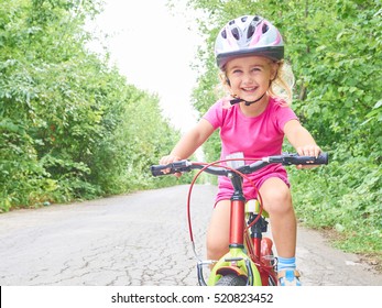 Happy Child Riding A Bike In Outdoor. Cute Kid In Safety Helmet Biking Outdoors. Little Girl On A Red  Bicycle  Healthy Preschool Children Summer Activity. 