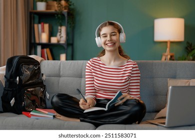 Happy child is sitting on sofa. Teenager girl is doing homework. - Powered by Shutterstock