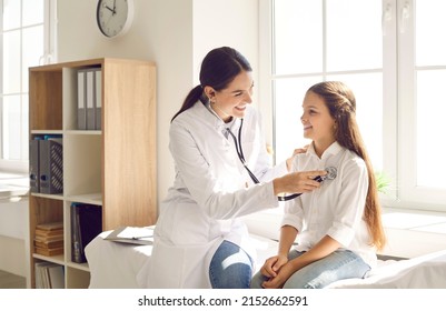 Happy Child Smiling While Doctor Is Examining Her Lungs Or Heart During Medical Checkup In Sunny Office. Cheerful Pediatrician Using Stethoscope To Check Respiration And Heartbeat Of Her Young Patient