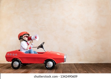 Happy Child Speaking To Megaphone At Home. Funny Kid Driving Toy Car Indoor. Success And Win Concept