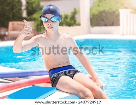 Happy child in sport goggles and cap showing thumbs up on the swimming pool background. Swim board, noodles near boy. Caucasian kid learning to swim and enjoying water. Healthy lifestyle. 