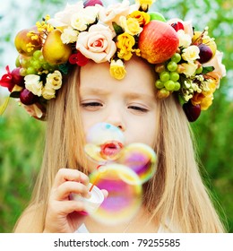 Happy Child in Summer. Beautiful Girl with Flowers Wreath from Flowers blows Soap Bubbles. Happy Children. Healthy Kids. Spring Time.