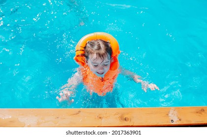 a happy child swims in the pool in a swimming orange vest - Shutterstock ID 2017363901