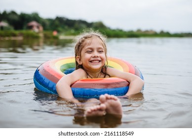Happy child swims in the river on a colored inflatable circle. Cute little girl gives birth while swimming in the lake. Summer vacation. - Shutterstock ID 2161118549