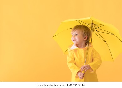 Happy Child Wearing Raincoat. Kid Holding Umbrella Against Yellow Background. Autumn Concept