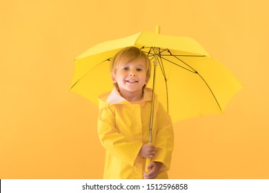 Happy Child Wearing Raincoat. Kid Holding Umbrella Against Yellow Background. Autumn Concept