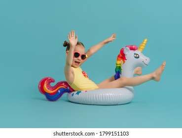 Happy Child Wearing Swimsuit. Girl With Swimming Ring Unicorn. Kid On A Colored Turquoise Background.