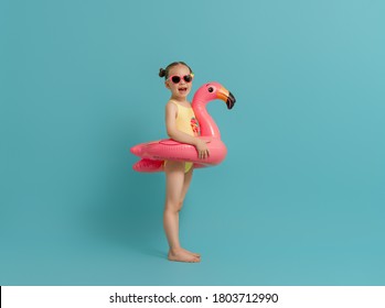 Happy Child Wearing Swimsuit. Girl With Swimming Ring Flamingo. Kid On A Colored Turquoise Background.