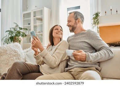 happy child-free couple with coffee cup and smartphone looking at each other on couch in living room - Powered by Shutterstock