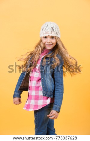 Happy childhood concept. Child model smile with long blond hair. Fashion, style, trend. Girl in jeans suit, hat, plaid shirt on orange background. Beauty, look, hairstyle.