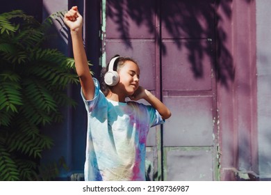 Happy childhood. A happy little girl listens to music and dances in the street. A small child wearing headphones. spring and autumn fashion. favorite music in headphones. generation z - Powered by Shutterstock