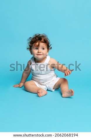 Happy childhood. Portrait of cute toddler boy, baby in white romper isolated over blue studio background. Concept of childhood, motherhood, life, birth. Copy space for ad