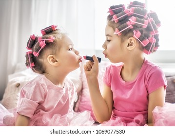 Happy childhood. Two sisters are doing hair and having fun. Children doing makeup sitting on the bed in the bedroom. - Shutterstock ID 1069077530