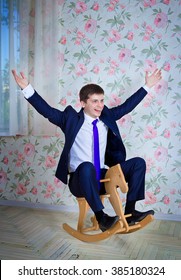 Happy Childish Young Man In Business Suit Riding Toy Wooden Horse. Adult Acting Like A Child Concept