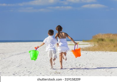 Happy Children, Boy Girl, Brother And Sister Running And Having Fun Playing In The Sand On A Beach With Bucket And Spade