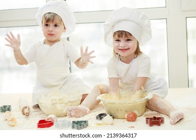 Happy children - a boy and a girl play in the kitchen with flour, children knead the dough, a child in a cook's costume, cooking from dough, playing cook.
