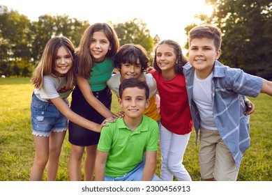 Happy children boys and girls from elementary school posing around friend and looking at camera with smile after joint walk in fresh air stand on lawn summer park. Kids event party concept - Powered by Shutterstock