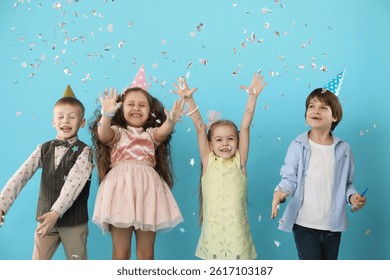 Niños felices en sombreros de papel cónico bajo el confeti que cae en fondo azul claro. Fiesta sorpresa de cumpleaños