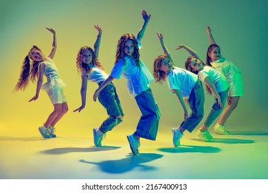 Happy children dancing. Group of children, little girls in sportive casual style clothes dancing in choreography class isolated on green background in yellow neon light. Concept of music, fashion, art - Powered by Shutterstock