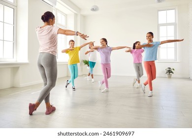 Happy children dancing. Group of little girls in sporty casual clothes are dancing in choreography class. Preteen girls rehearse dance moves with their female coach at children's dance studio. - Powered by Shutterstock