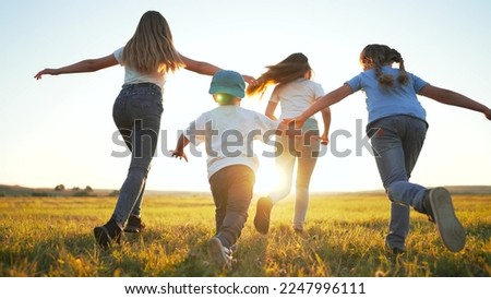 Happy children with dog run together on green field of park at sunset. Rear view of children running across field. crowd of children with dog run along green grass in summer park. Happy childhood.