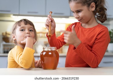 Happy Children Eating Honey From A Jar At Home In The Kitchen. Funny Girls Lick Honey From A Spoon. Healthy Organic Food Sweets For Kids