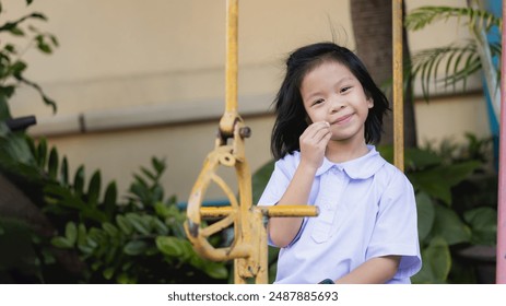 Happy children enjoying summer activities in the park. Asian girl is sitting on a swing on sunny day, Child sweet smiling and looking at the camera, Kid wearing school uniform, a seven year old child. - Powered by Shutterstock