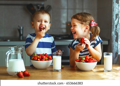 Happy children girl and boy brother and sister eating strawberries with milk