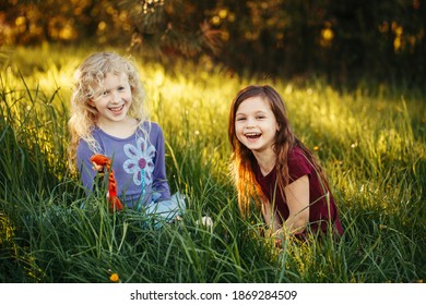Happy children girls playing dolls in park. Cute adorable kids sitting in grass on meadow playing toys. Happy childhood authentic lifestyle. Outdoor summer activity for kids.