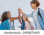 Happy children giving high five each other standing near school outdoors. Primary education friendship childhood people concept. Group of kids classmates students friends making high five at yard