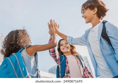 Happy children giving high five each other standing near school outdoors. Primary education friendship childhood people concept. Group of kids classmates students friends making high five at yard