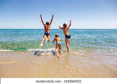 Happy children having fun on a beach running and jumping to the sea enjoying summer vacation