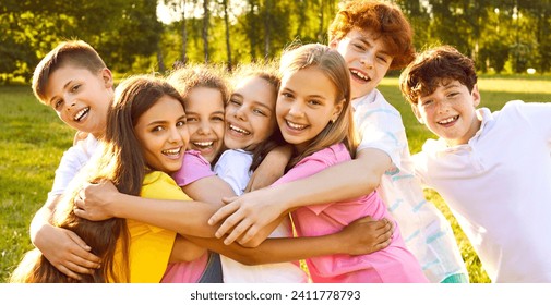 Happy children having fun on summer vacation. Group of best friends playing outdoors together. Several little kids, girls and boys with backlit hair, hugging each other tightly in a green sunny park - Powered by Shutterstock