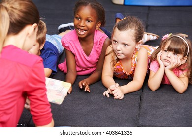 Happy children listening to fairytale book in preschool read by nursery teacher