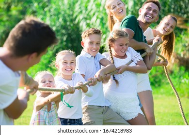 Happy  children with parents playing active games in summer park, tugging war