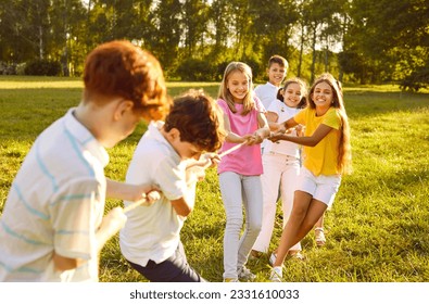 Happy children play games in park on sunny summer day. Cheerful kids meet on green field or meadow, hold rope, play tug of war, compete with each other, enjoy challenge, make effort. Teamwork concept - Shutterstock ID 2331610033