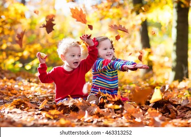 Happy children playing in beautiful autumn park on warm sunny fall day. Kids play with golden maple leaves. Focus on girl.