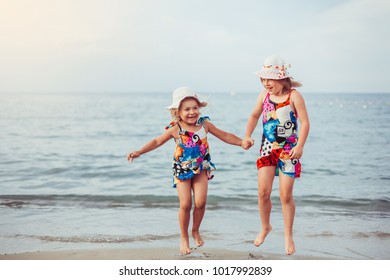 Happy children playing, jumping and holding hands on the beach coast. Kids sisters having fun outdoors. Summer vacation and healthy lifestyle concept