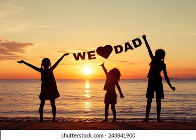 Happy children playing on the beach at the sunset time. Children hold in the hands  inscription "We love dad". Concept of happy father day.