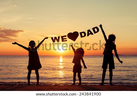 Happy children playing on the beach at the sunset time. Children hold in the hands  inscription "We love dad". Concept of happy father day.