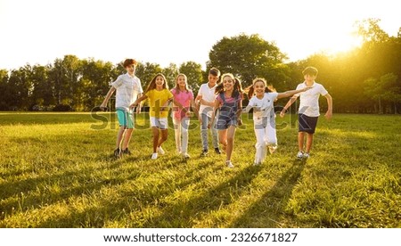 Happy children playing in the park in summer. Group of cheerful kid friends playing active outdoor games, running on a green grassy lawn, having fun and enjoying free time