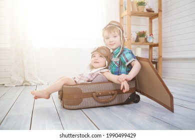 Happy children playing with vintage wooden airplane. Kids having fun at home. Imagination and freedom concept. Two little children wearing pilot costume and playing with old suitcase
