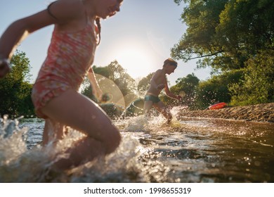 Happy children run from the shore into the water. Summer children's vacation on shore of a lake or river. boy and girl jump into water, swim and splash around at sunset. Active holidays. Dynamic image - Powered by Shutterstock