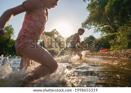 Happy children run from the shore into the water. Summer children's vacation on shore of a lake or river. boy and girl jump into water, swim and splash around at sunset. Active holidays. Dynamic image