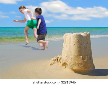 Happy Children Running On Beach By Sand Castle