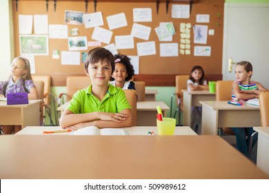 Happy children sitting in class and classmates in the background, doing schoolwork