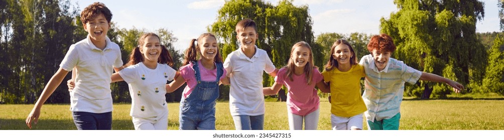 Happy children standing in a line together outside and smiling in the park on holidays enjoying spending time in a summer camp. Portrait of a hugging kids looking outdoor at the camera. Banner. - Powered by Shutterstock