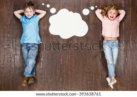 Happy children. Top view creative photo of little boy and girl on vintage brown wooden floor. Children lying near empty cloud with thoughts, looking at camera and smiling
