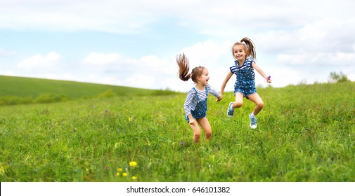 Happy Children Twins Sisters Jumping And Laughing On The Meadow In Summer