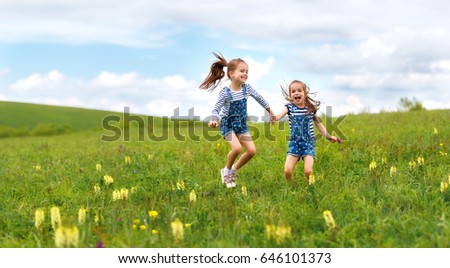 happy children twins sisters jumping and laughing on the meadow in summer